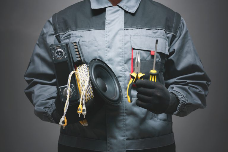 A imagem mostra uma pessoa do pescoço para baixo segurando algumas ferramentas como alicate e chave de fenda fazendo referência a como instalar um equipamento de som.